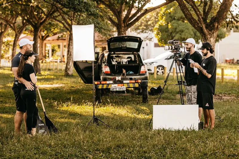 Small film crew with a camera and lights shooting on a park lawn